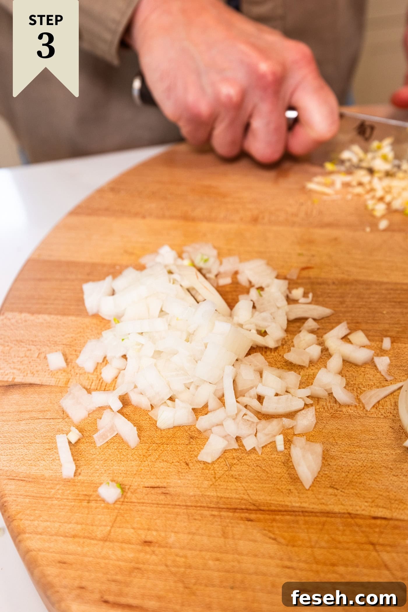 Chopped onion sitting on a wooden cutting board before being cooked.