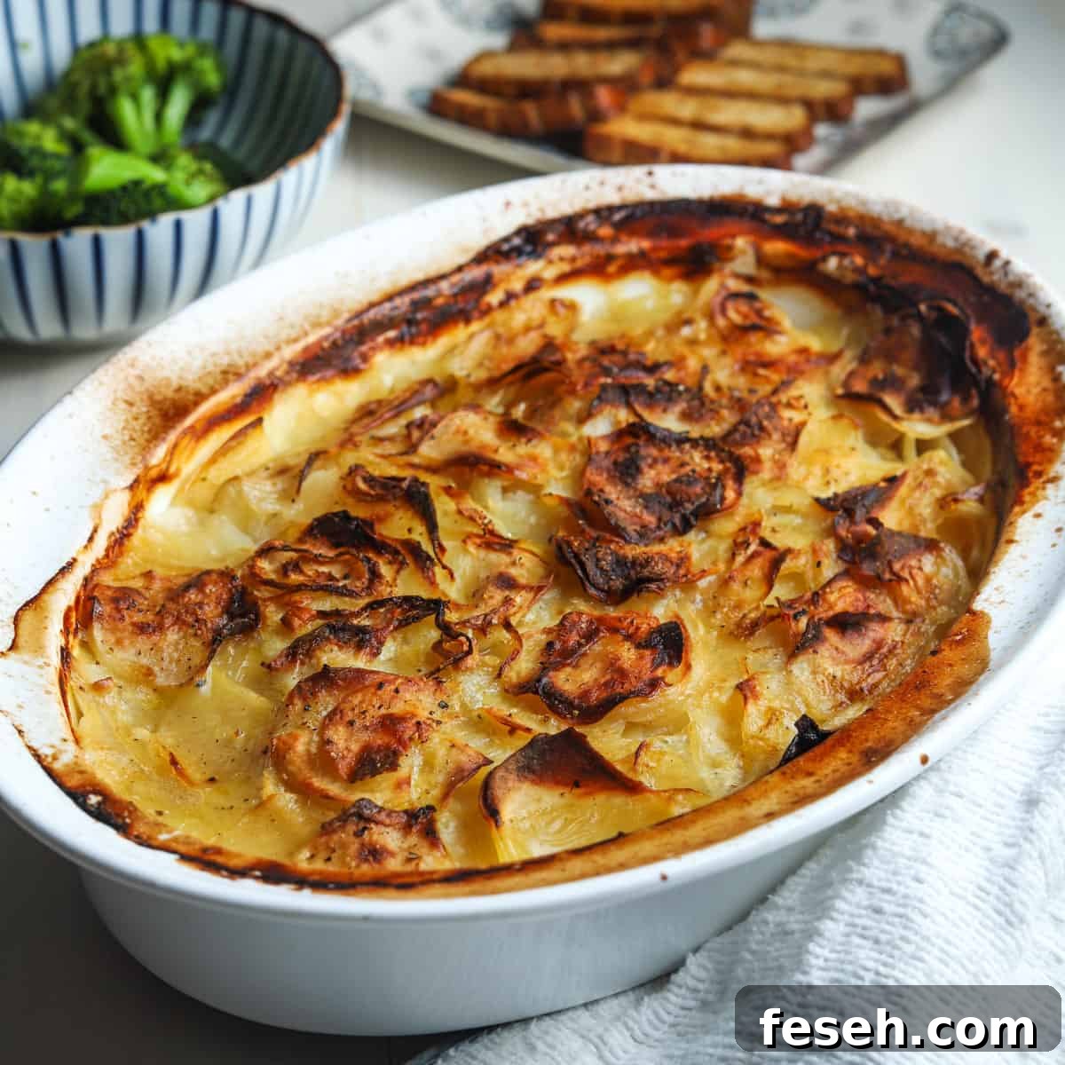 Photo of vegan boulangere potatoes in a dish with dishes of broccoli and smoked tofu slices in the background.