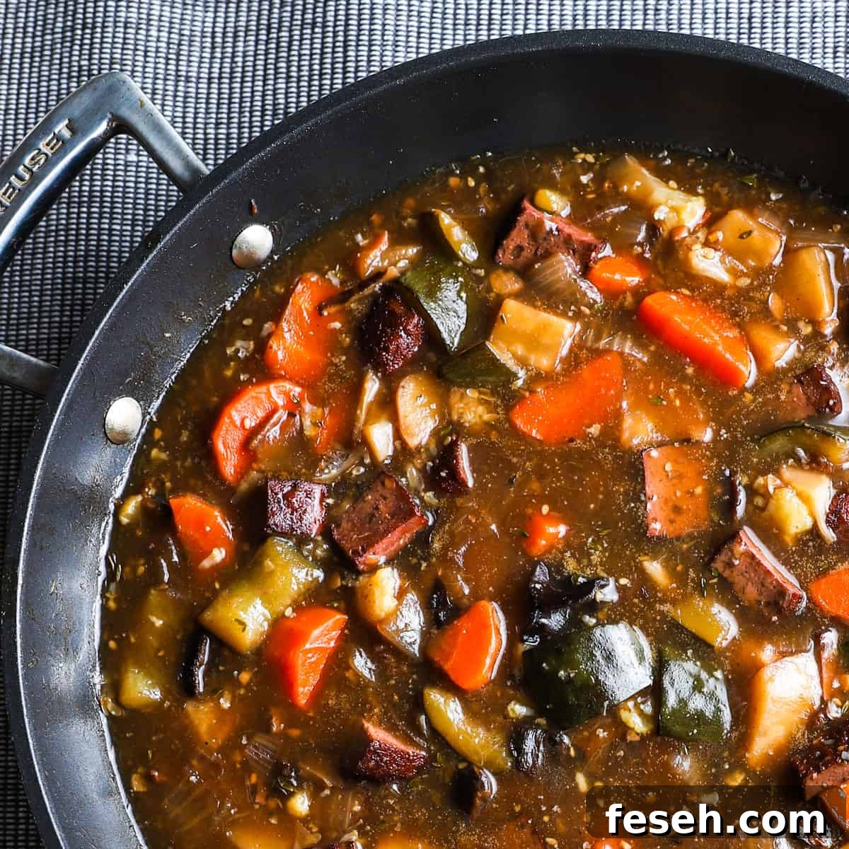 1x1 photo of vegan stew in a black large saute pan on a grey textured table cloth.