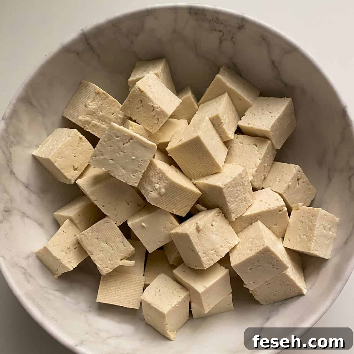 photo of a white bowl full of cubes of raw tofu.