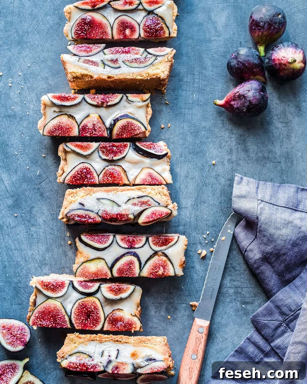 Fig tart cut into slices next to knife, figs and linen napkin on table.