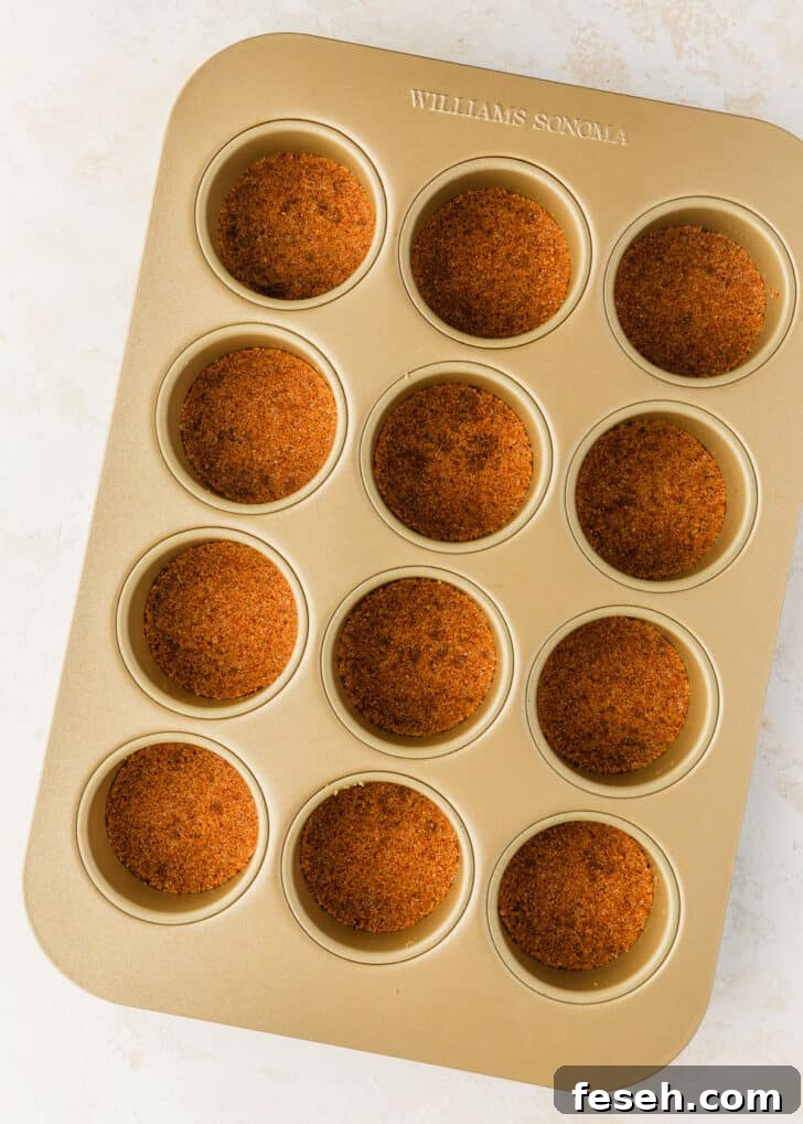 A mini cheesecake pan with graham cracker crusts on a tan counter.