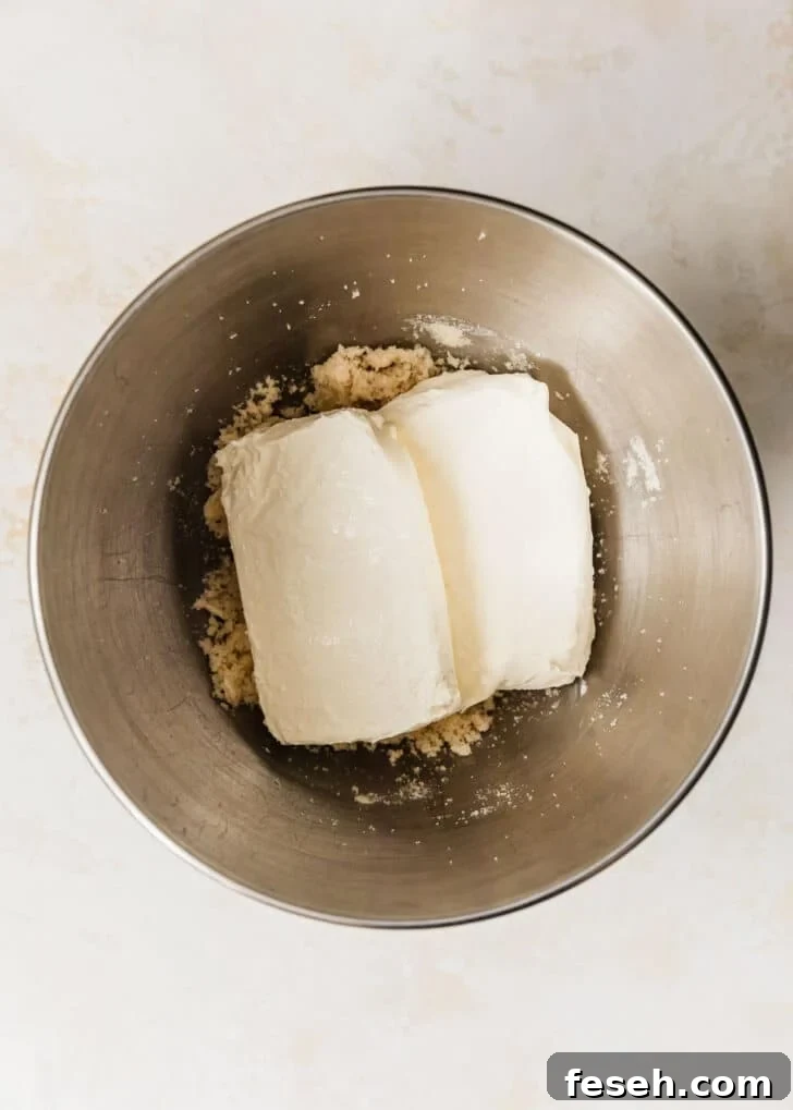 A silver bowl of cream cheese, butter, & sugar on a tan counter.