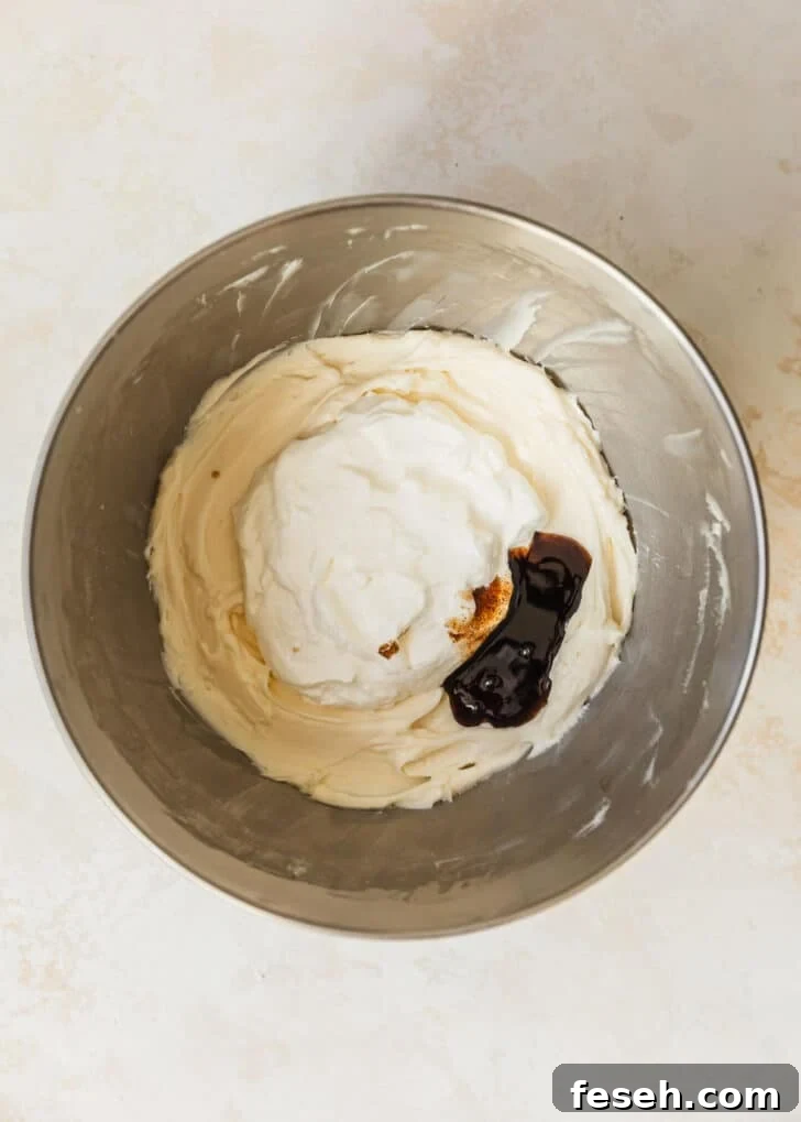 A silver bowl of cream cheese, sour cream, and vanilla on a tan counter.