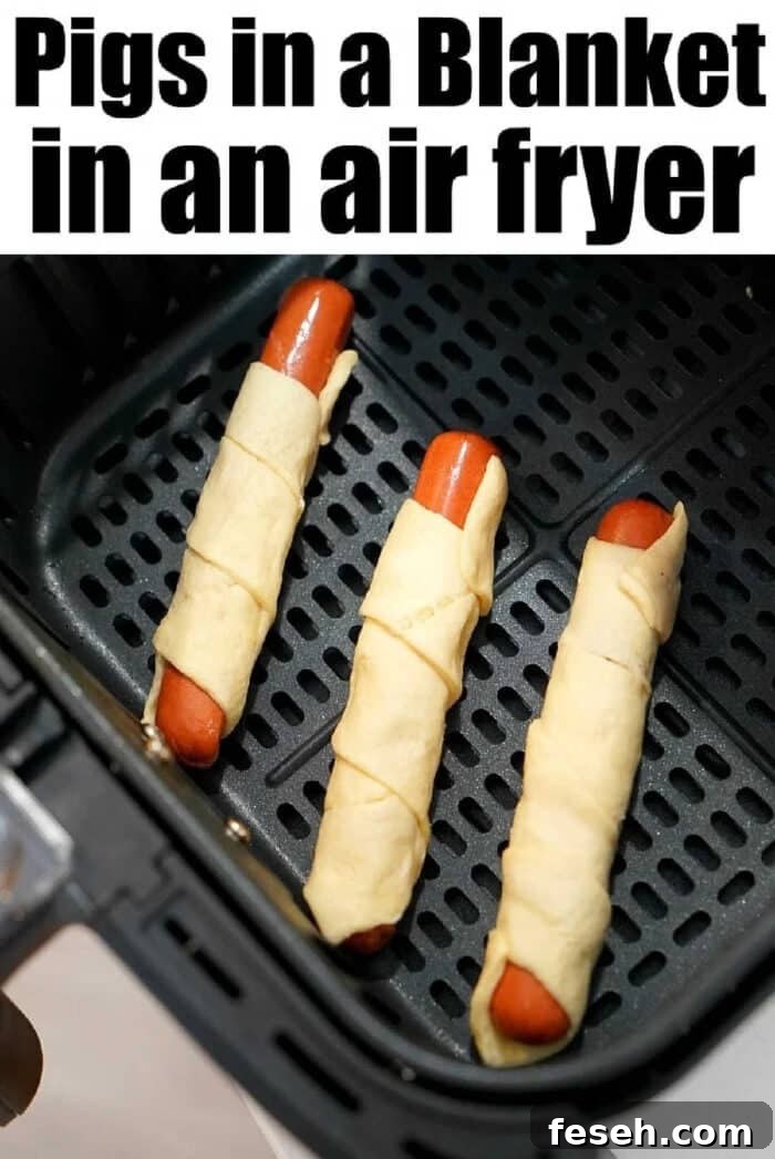 Three air fryer pigs in a blanket sit perfectly arranged in the basket, ready to be cooked to golden perfection.