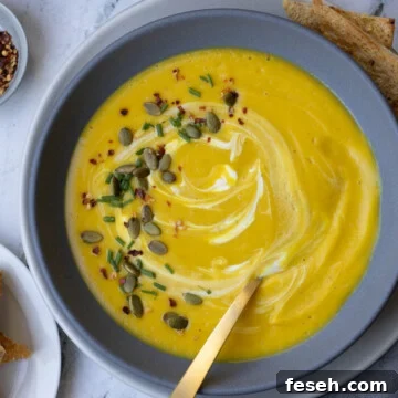 Creamy squash and apple soup in a gray bowl with pumpkin seeds and chives.