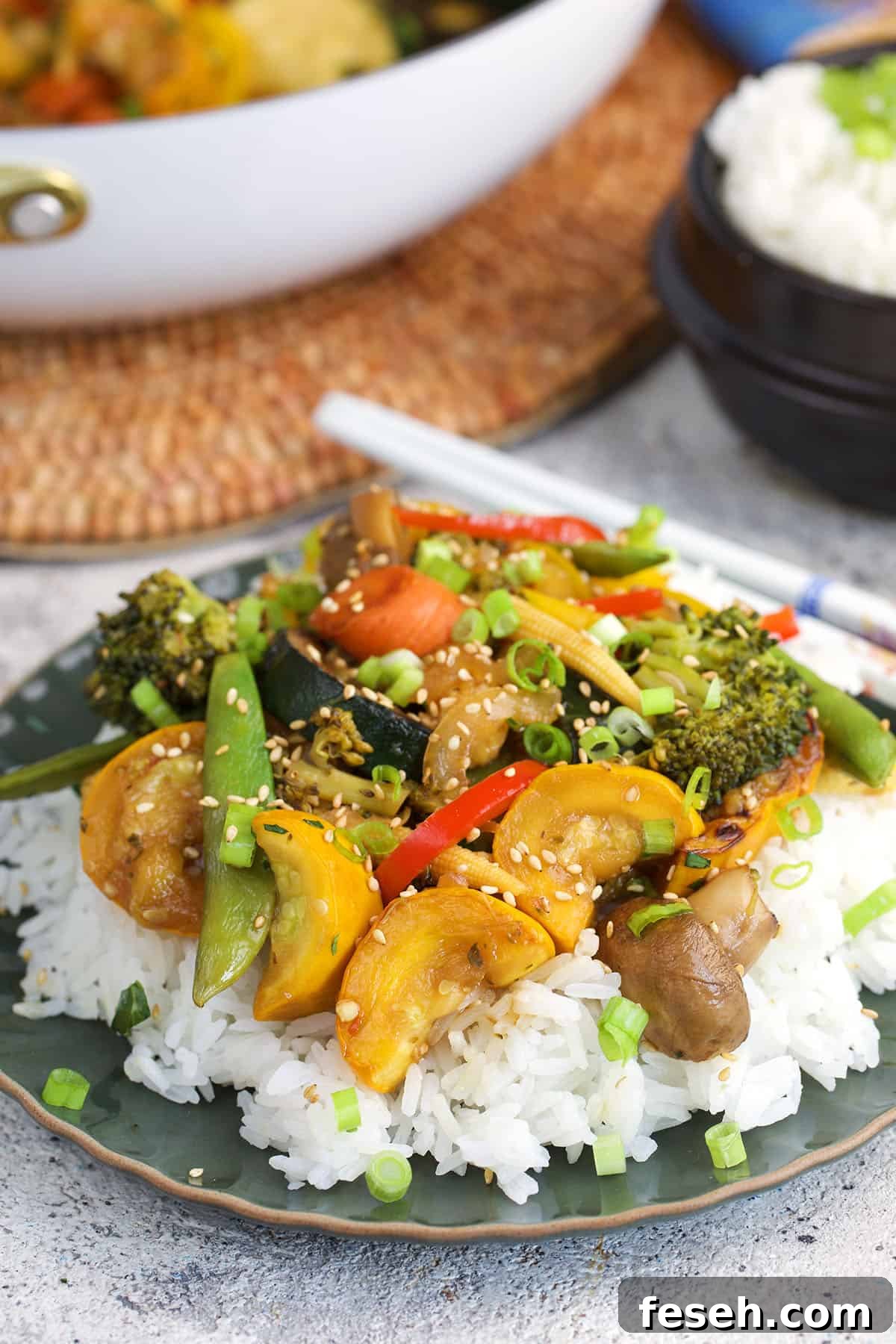 Stir Fried Vegetables on a bed of rice plates on a green plate with white chopsticks.