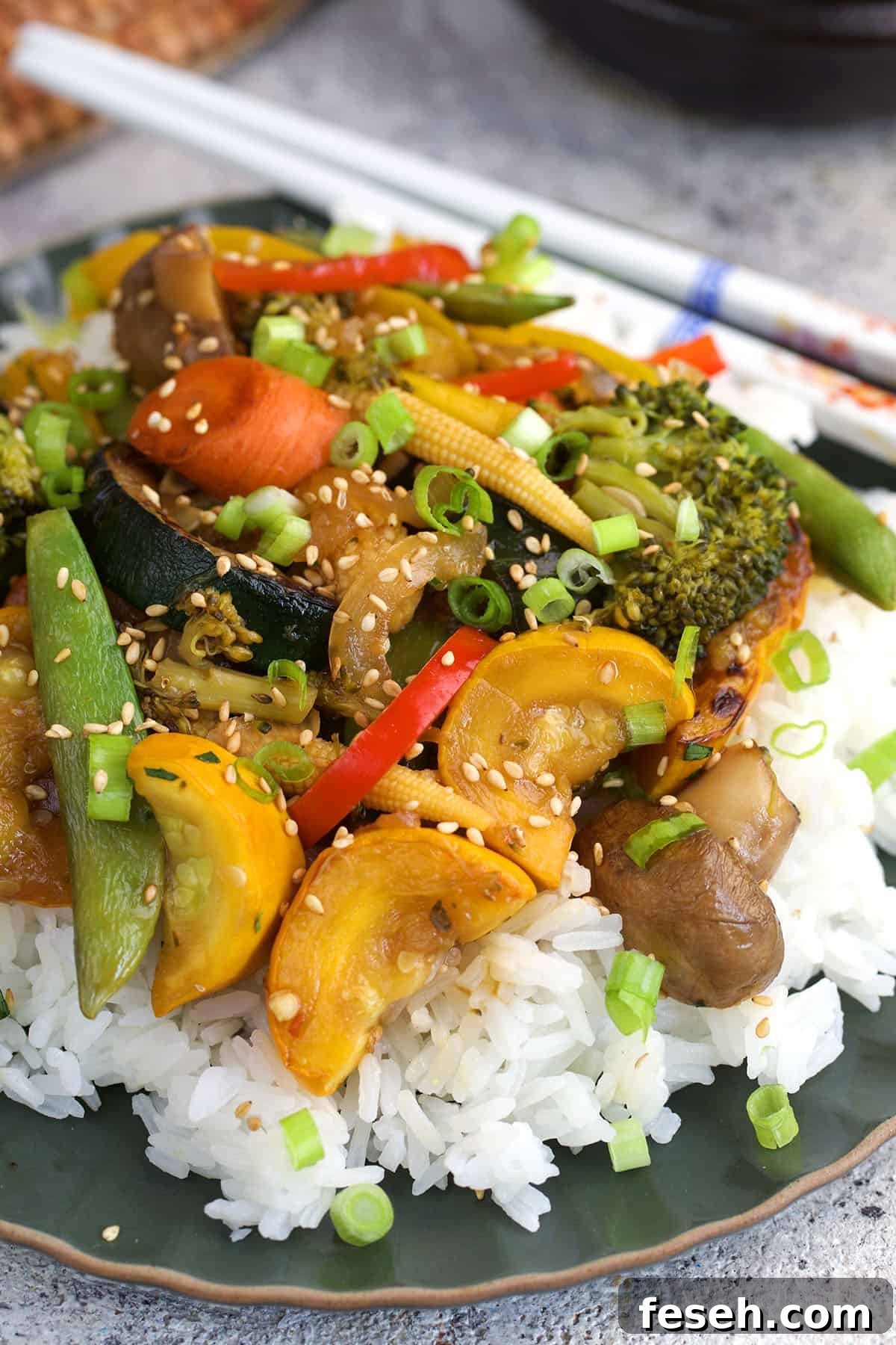 vegetable stir fry on white rice with white chopsticks next to it