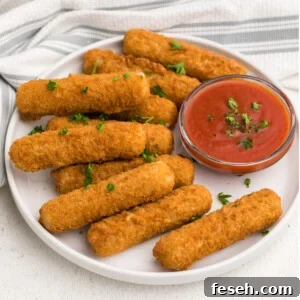 Frozen Air Fryer Mozzarella Sticks on a white plate with dipping sauce and topped with fresh parsley.