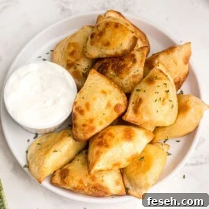 Golden and puffy, air fryer pierogies served on a white plate with a side of sour cream.