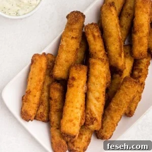 Golden fish sticks stacked on a white plate with a side of tartar sauce