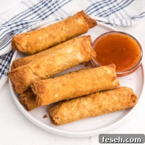 Egg rolls on a white plate with a side of dipping sauce.