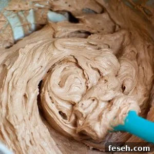 Mixing fluffy chocolate frosting in a mixing bowl with a blue spatula.