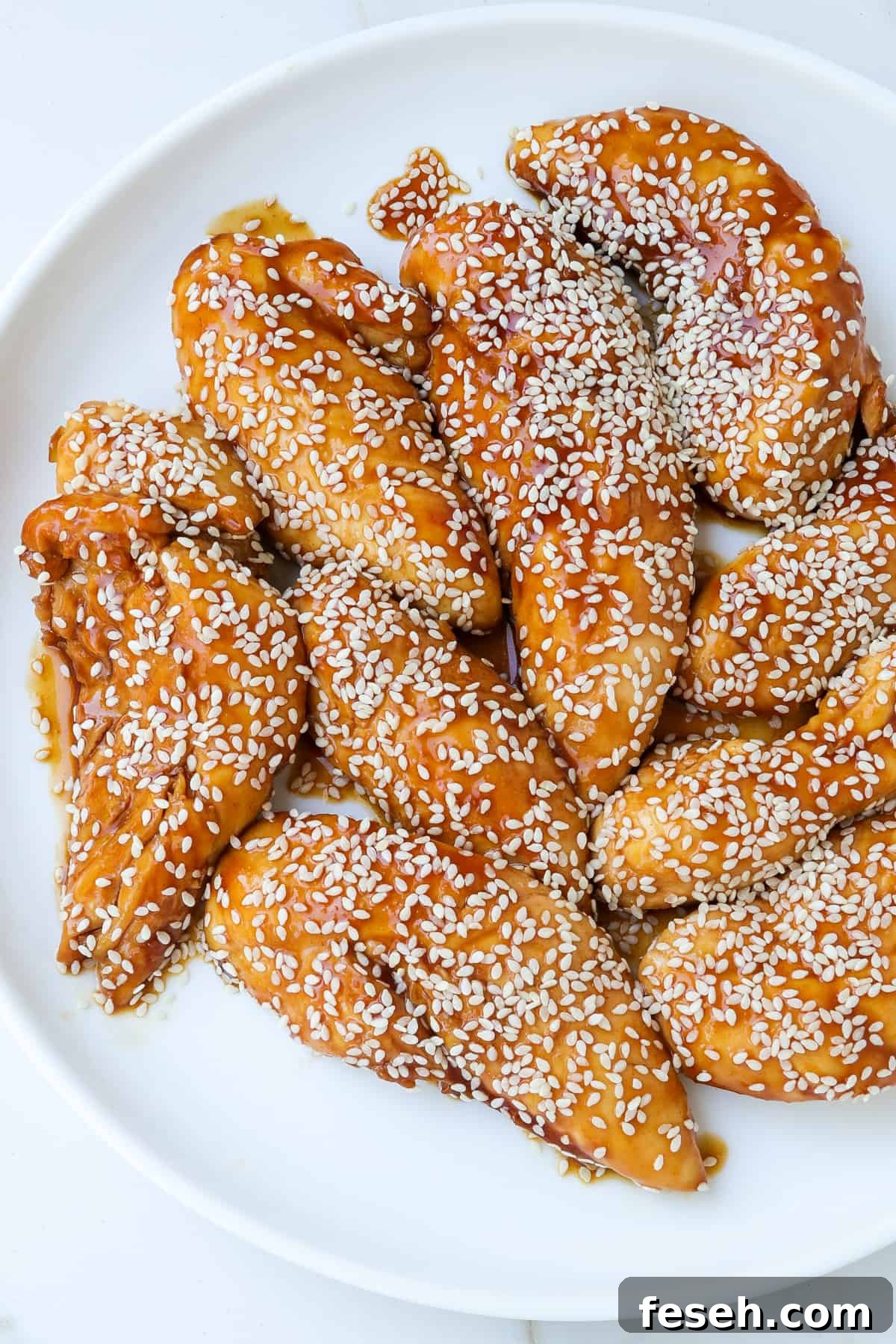 Close up shot of air fryer teriyaki chicken pieces on a plate with sesame seeds sprinkled on top.