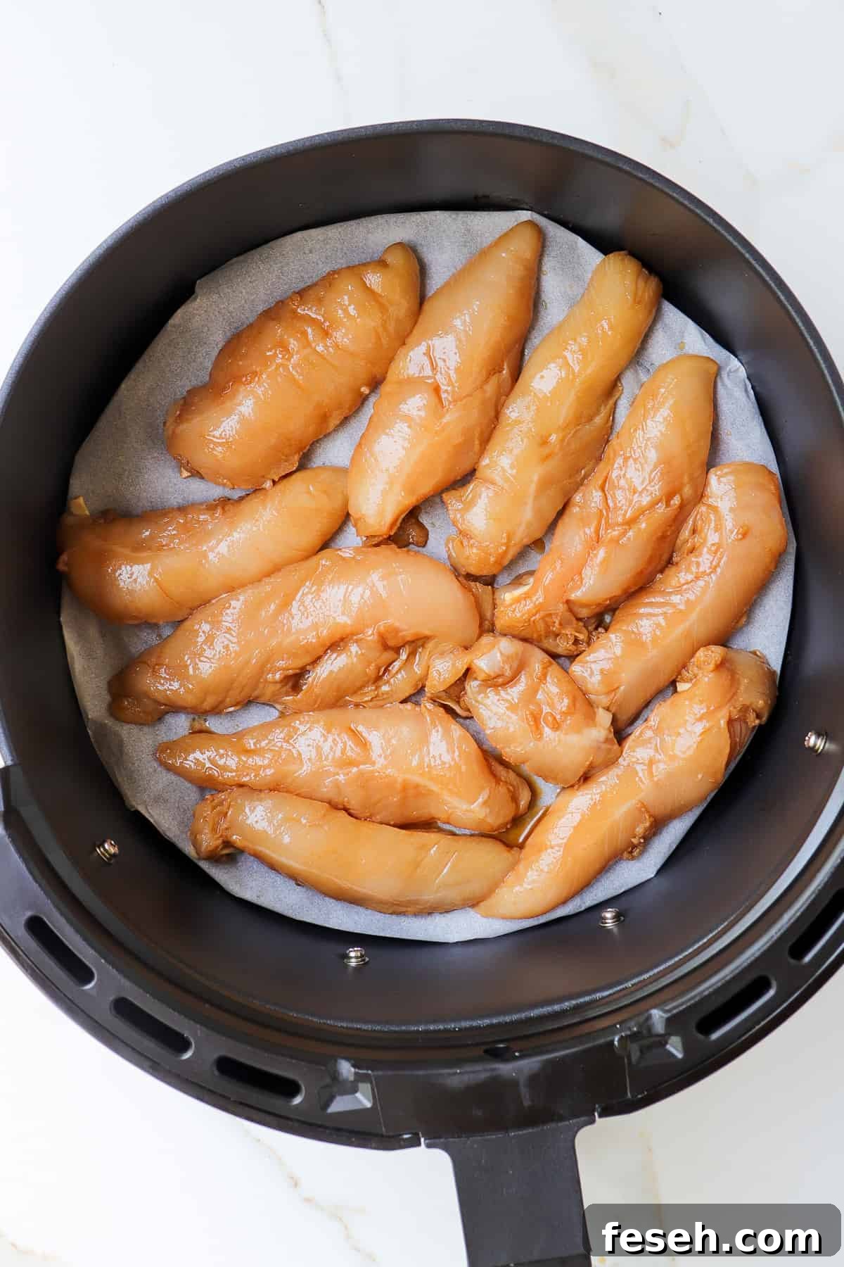 Marinated chicken pieces in air fryer basket.