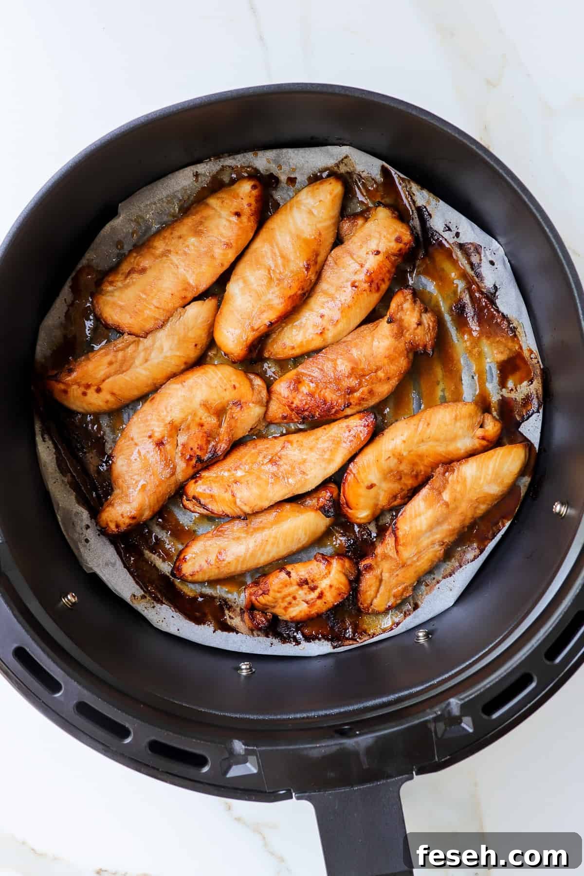 Cooked chicken pieces in air fryer basket.