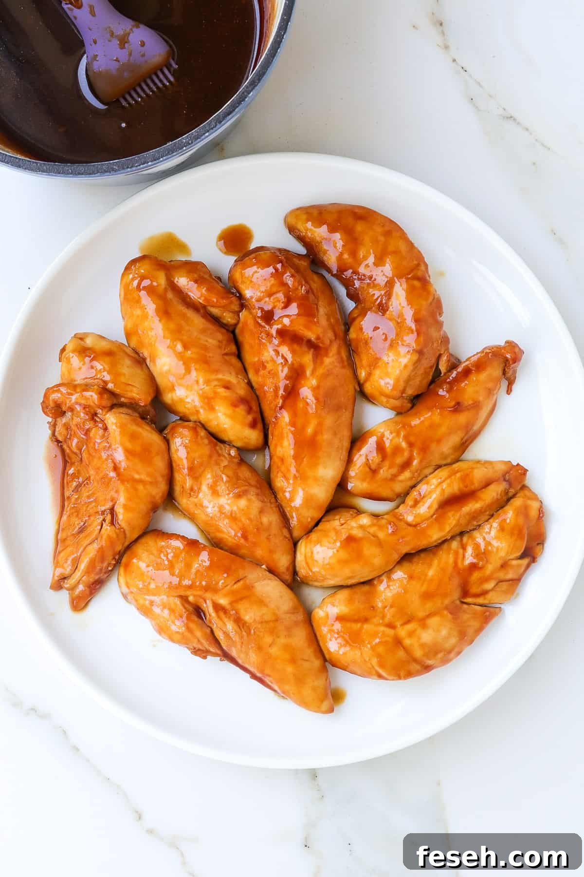 Cooked air fryer chicken tenders on a plate with a small saucepan of teriyaki sauce on the side.