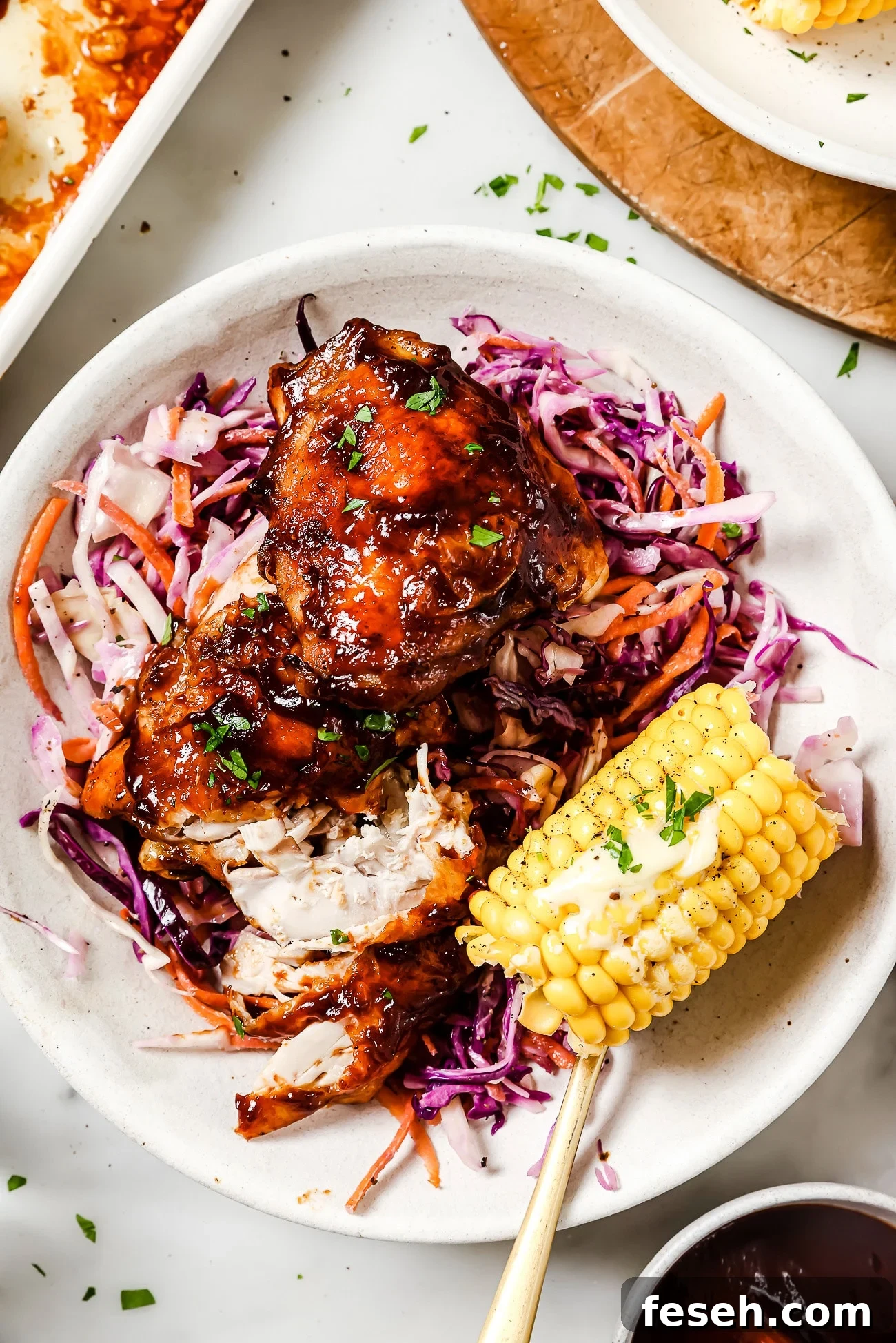 Baked BBQ chicken thighs on a plate with coleslaw and corn.