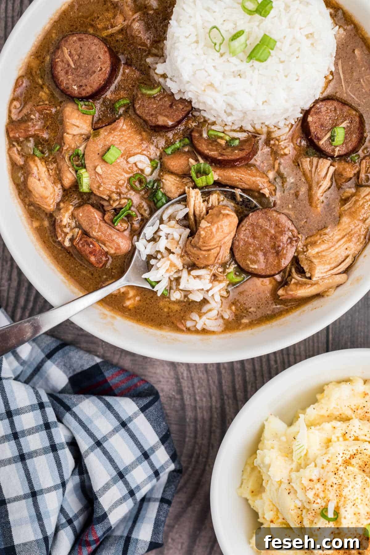a bowl of chicken sausage gumbo with a spoon hanging out of it with rice in the middle, a potato salad on the side