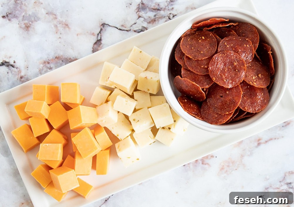 keto pepperoni in a white bowl next to two piles of cubed cheese