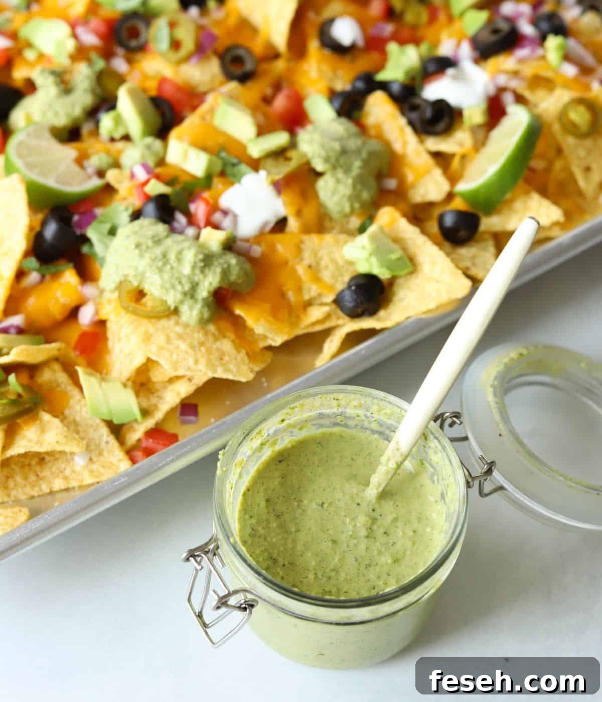 jar of creamy poblano sauce with spoon in it with nachos in background