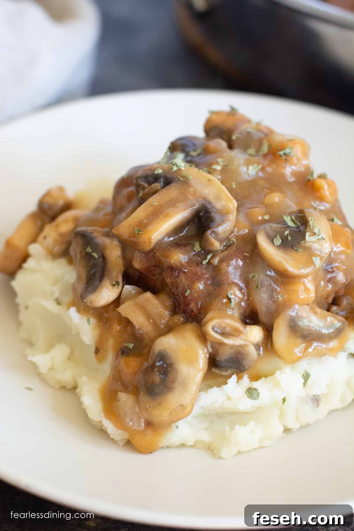 A serving of gluten-free salisbury steak with mushrooms and onions served over mashed potatoes.