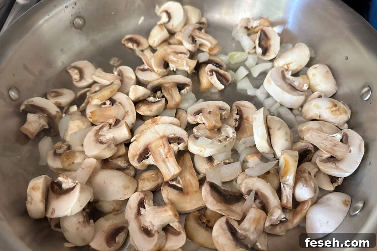 Sliced mushrooms and onions cooking in a large pan.
