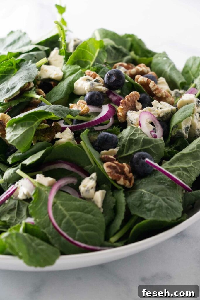 A large bowl of salad greens with blueberries, red onion slices roasted walnuts and blue cheese.