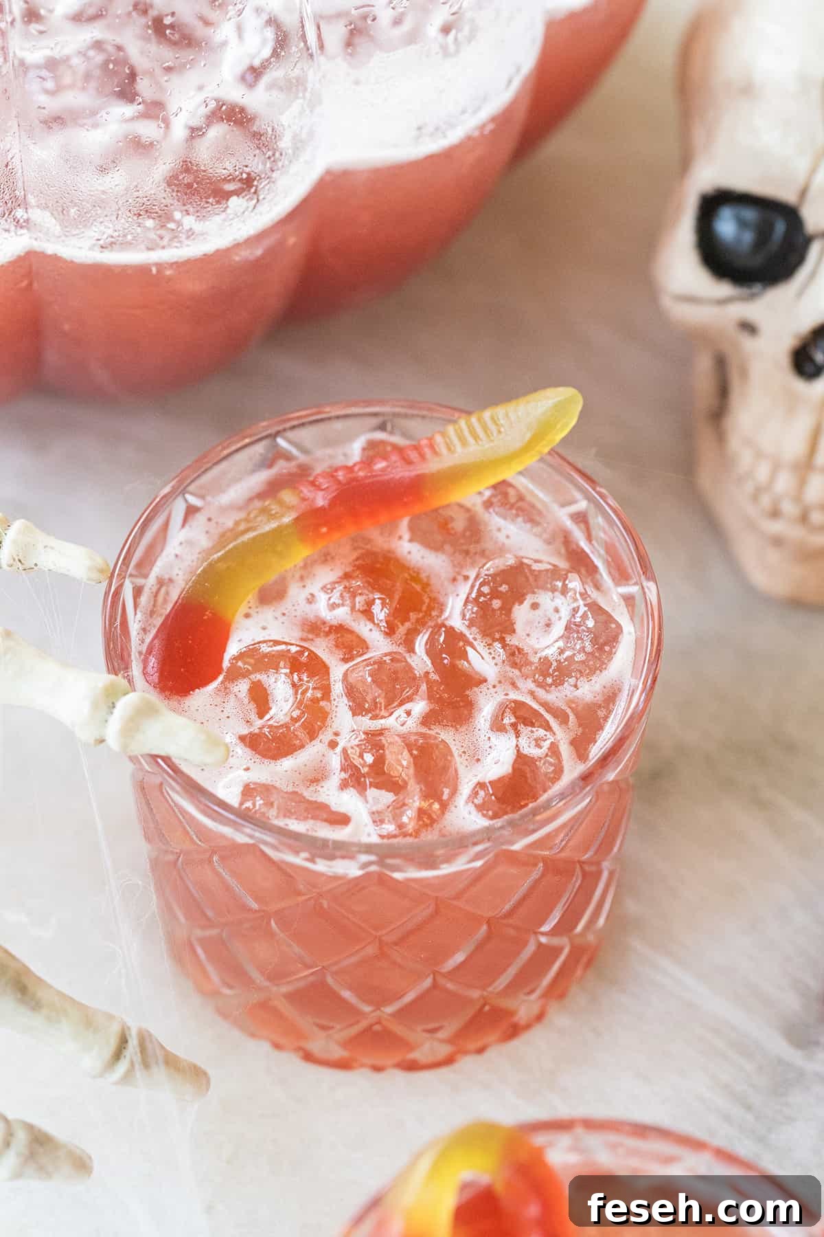 Pink Halloween punch non-alcoholic drink in a glass with a gummy worm and skeleton hand.