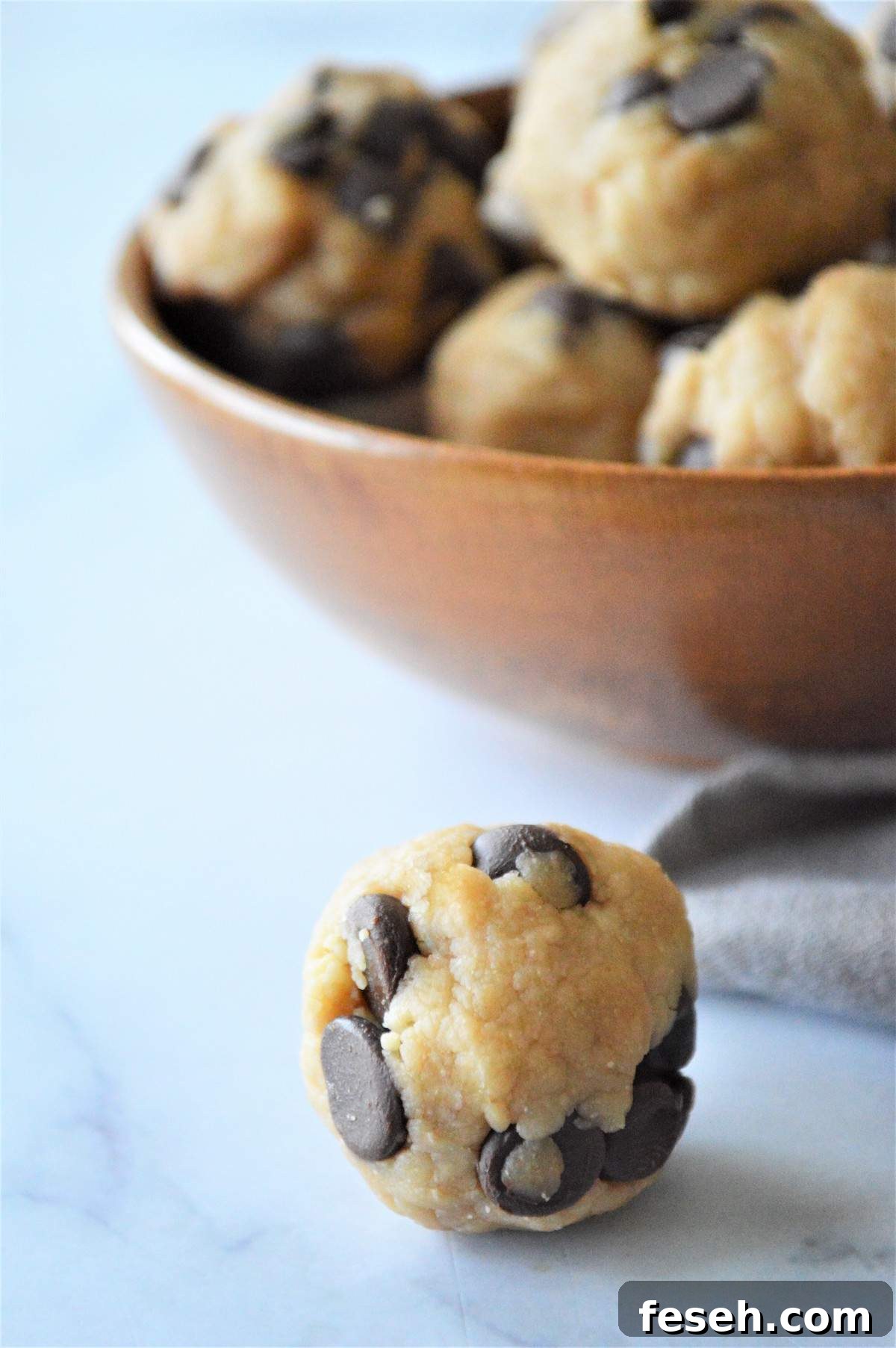A cookie dough energy bite in front of a bowl of energy bite.