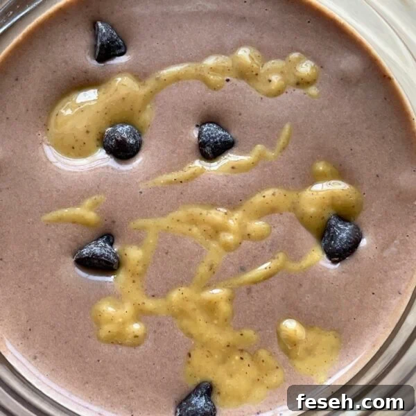 A chocolate peanut butter and banana smoothie with peanut butter drizzled over the top and chocolate chips sprinkled around.
