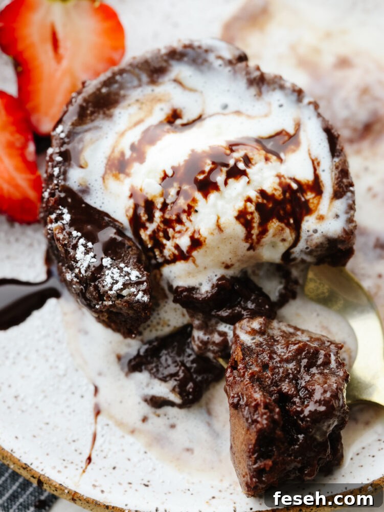 A close up of chocolate lava cake with melting ice cream and a spoon cutting into it.