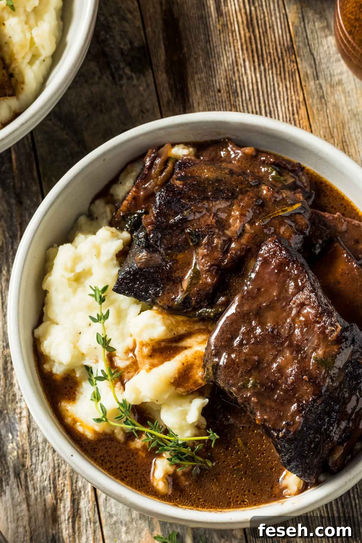 a dish of braised beef short ribs over mashed potatoes with a sprig of fresh thyme