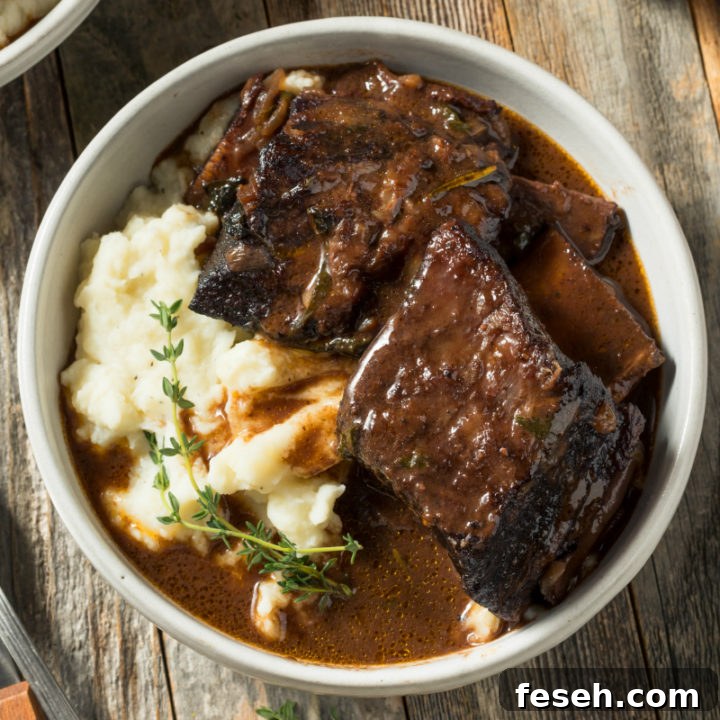 a white bowl with a serving of braised beef short ribs over creamy mashed potatoes, then topped with a fresh sprig of thyme