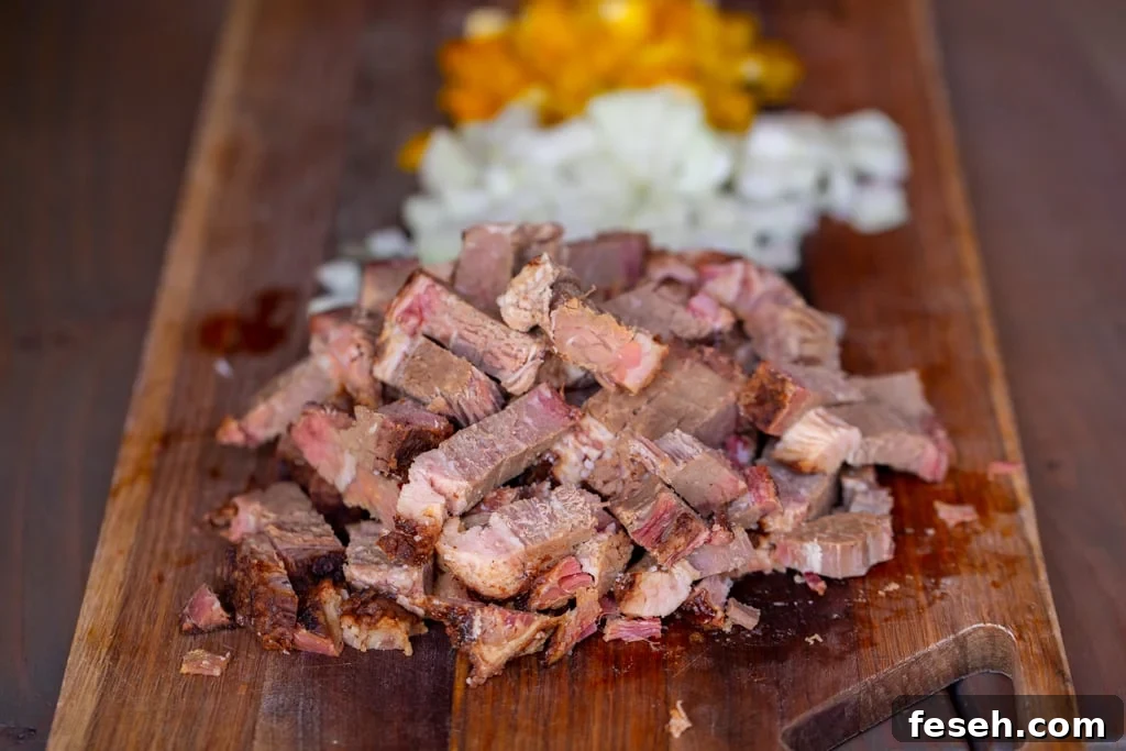Chopped beef brisket, onions, and peppers on a wooden cutting board.