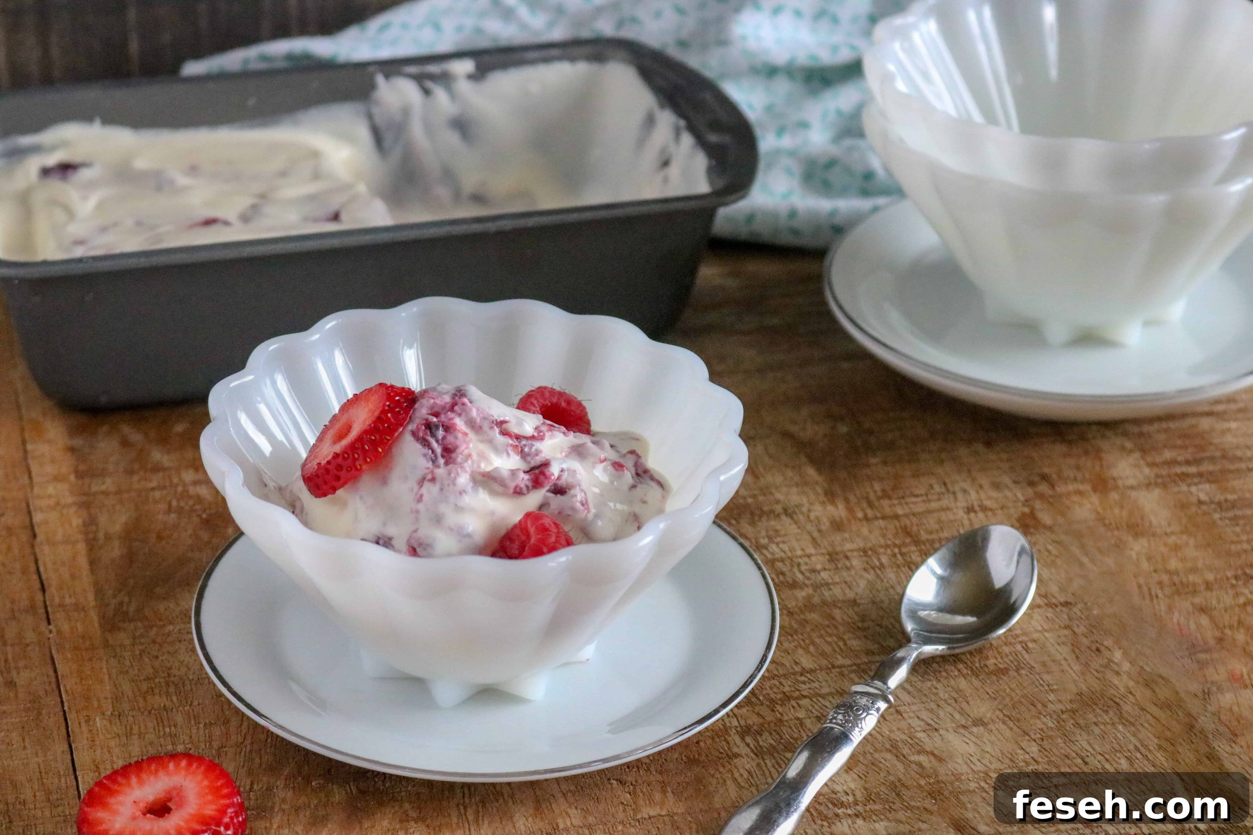 Berry Pie No-Churn Ice Cream in a white scalloped bowl on a white saucer next to a silver spoon and a strawberry slice on the table