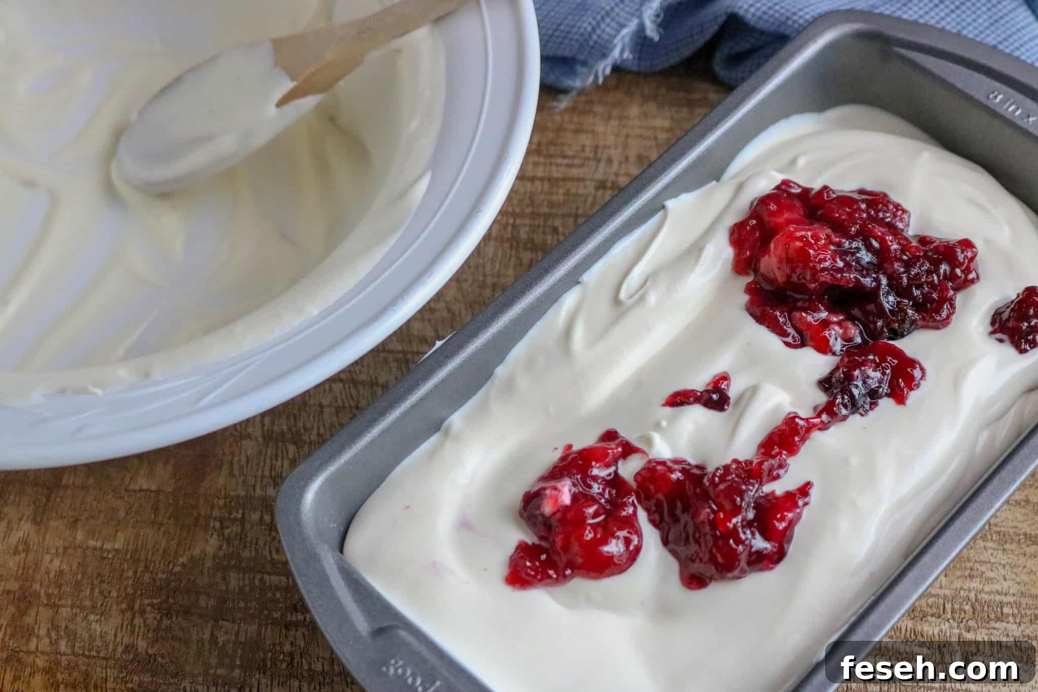 White bowl with wooden spoon in it next to a silver pan filled with No-Churn Ice Cream with berry pie filling swirled on top