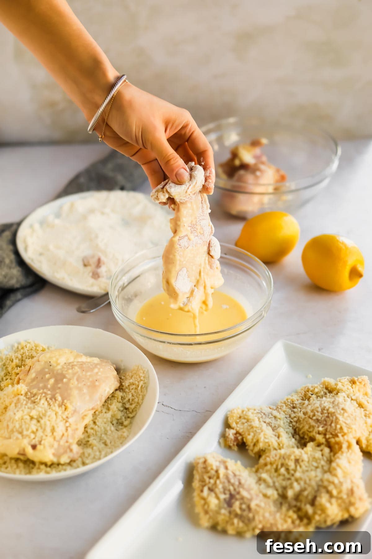 Raw chicken being dipped into egg mixture with lemons, flour, and panko