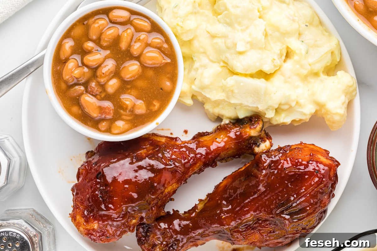 2 chicken drumsticks on plate with mashed potatoes and container of beans.