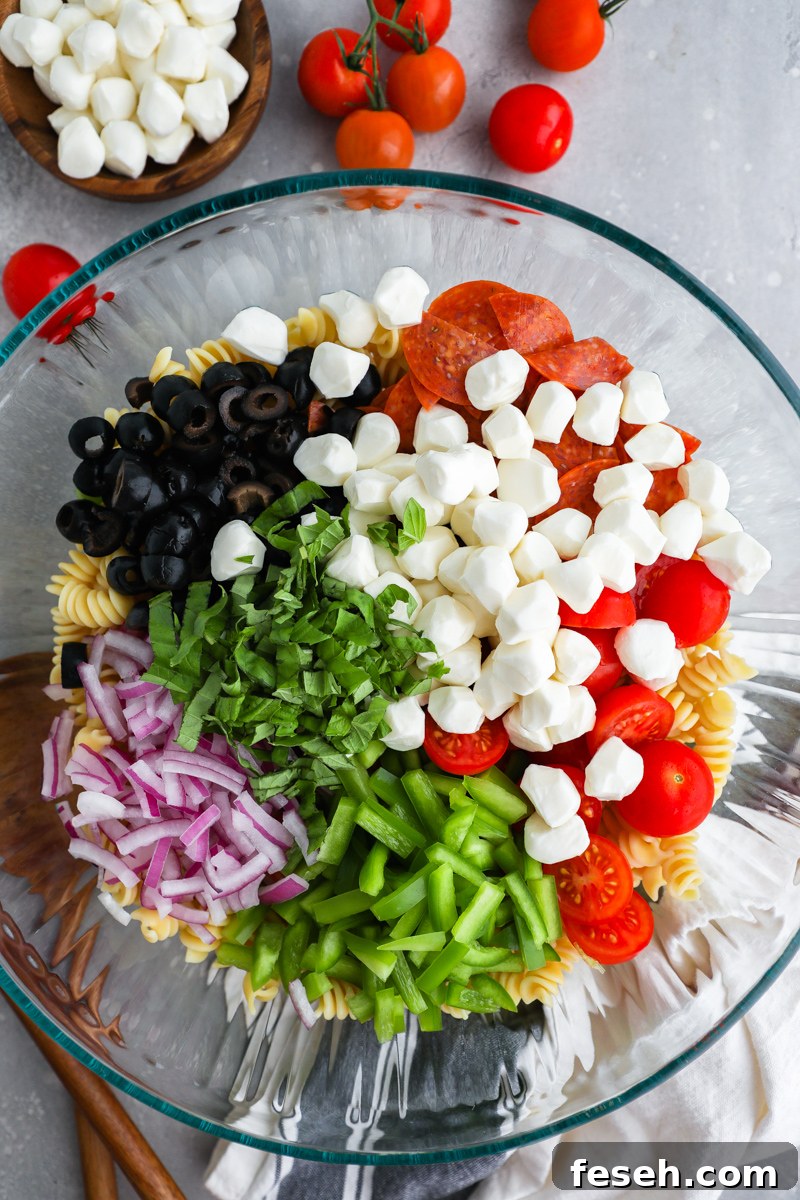 A clear bowl filled with ingredients to make a pizza pasta salad