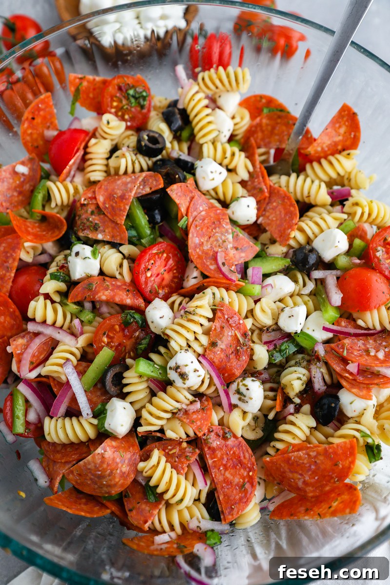 A large clear mixing bowl filled with pizza pasta salad freshly tossed in a zesty homemade Italian dressing