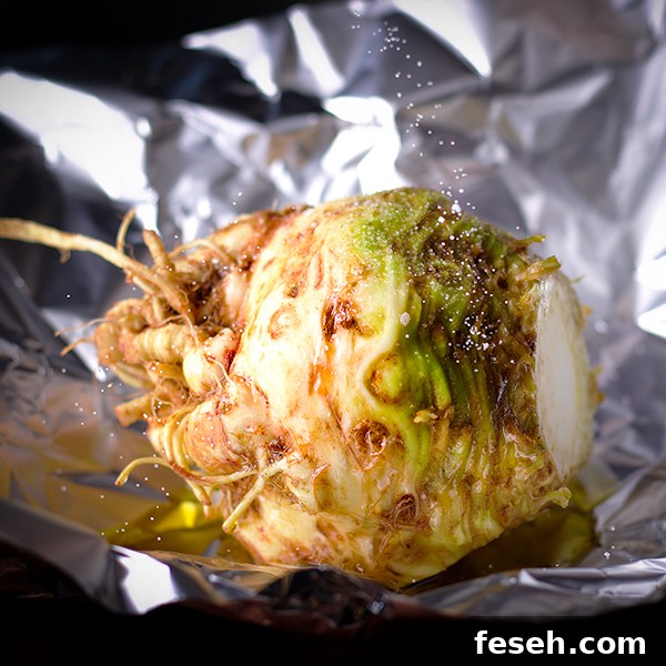 Sprinkling salt onto a whole celery root on a piece of aluminum foil.