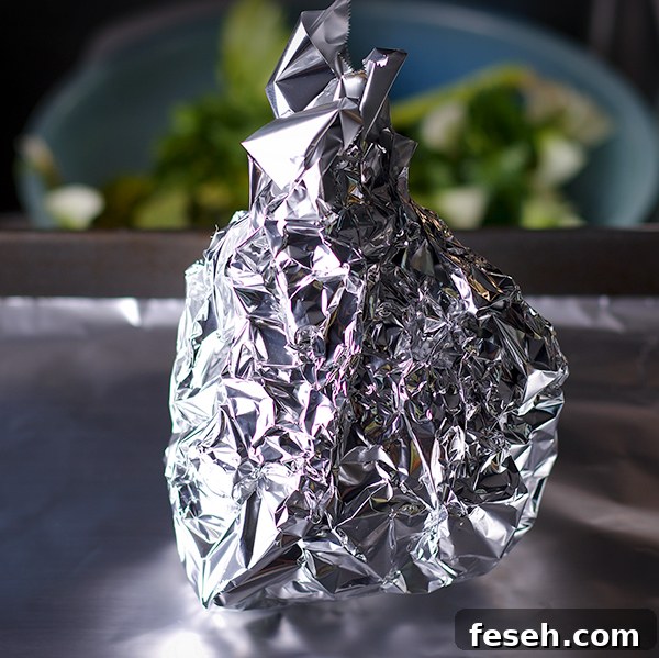 A whole celery root wrapped in aluminum foil, ready to roast.