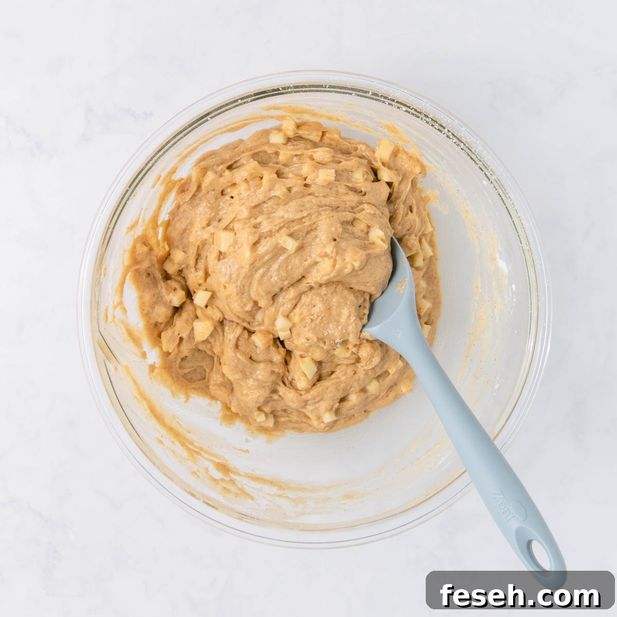 The mixed muffin batter with chunks of apple evenly mixed in.