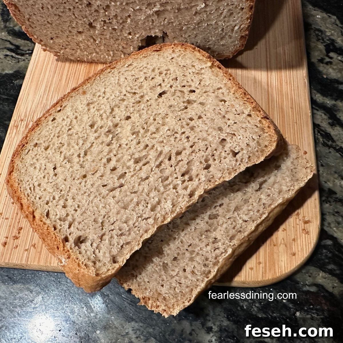A photo of a loaf baked in my bread machine. There are two slices of bread on the cutting board.
