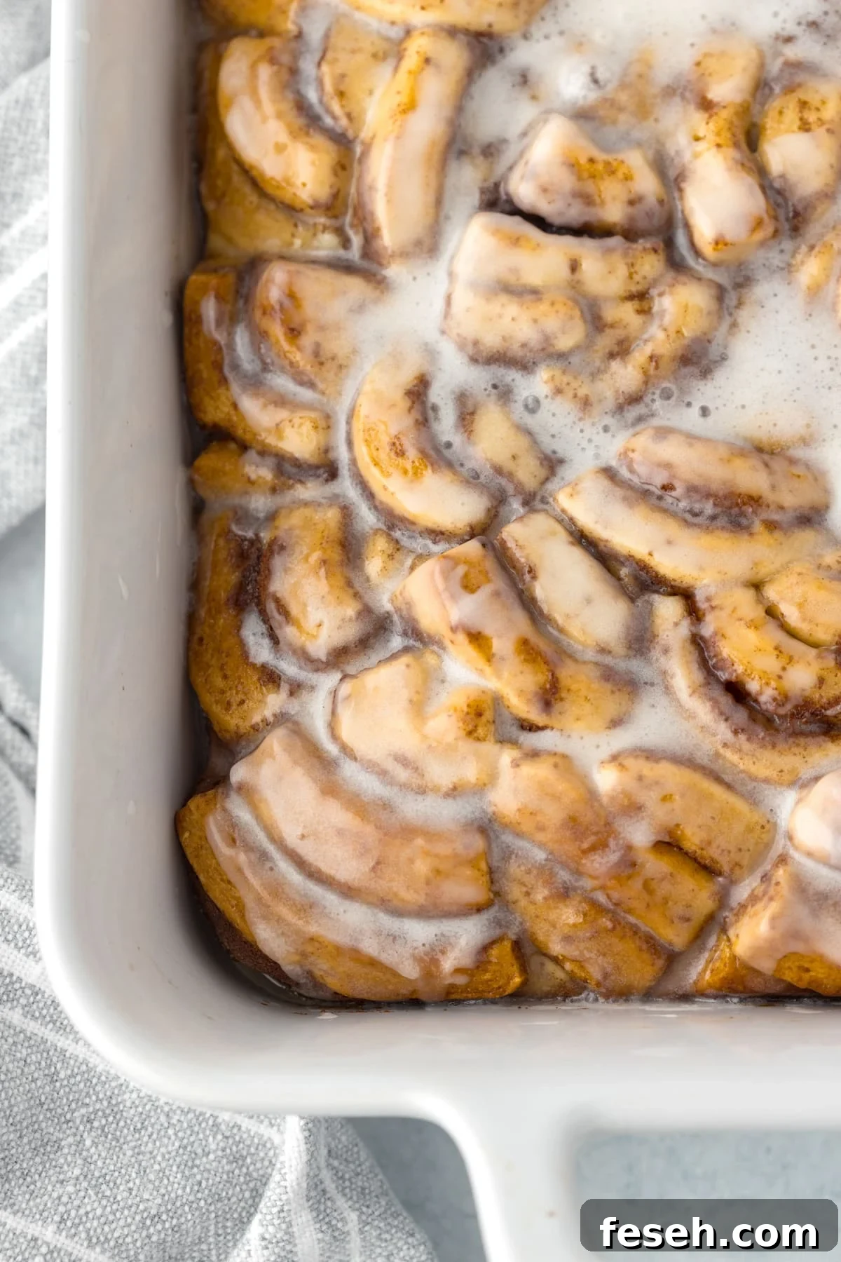 A baking dish filled with cinnamon roll pieces, baked and topped with icing.