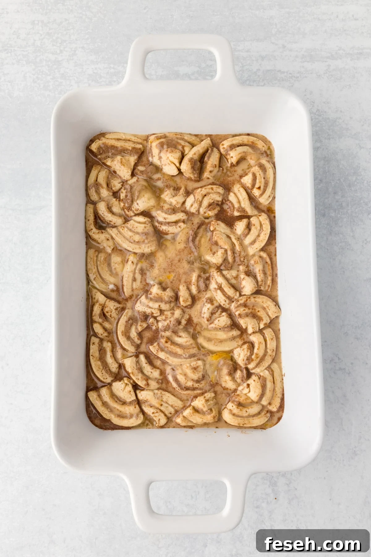 A baking dish with sliced cinnamon rolls and a custard base in it.