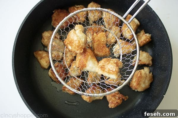 Chicken in a strainer over the top of black skillet.