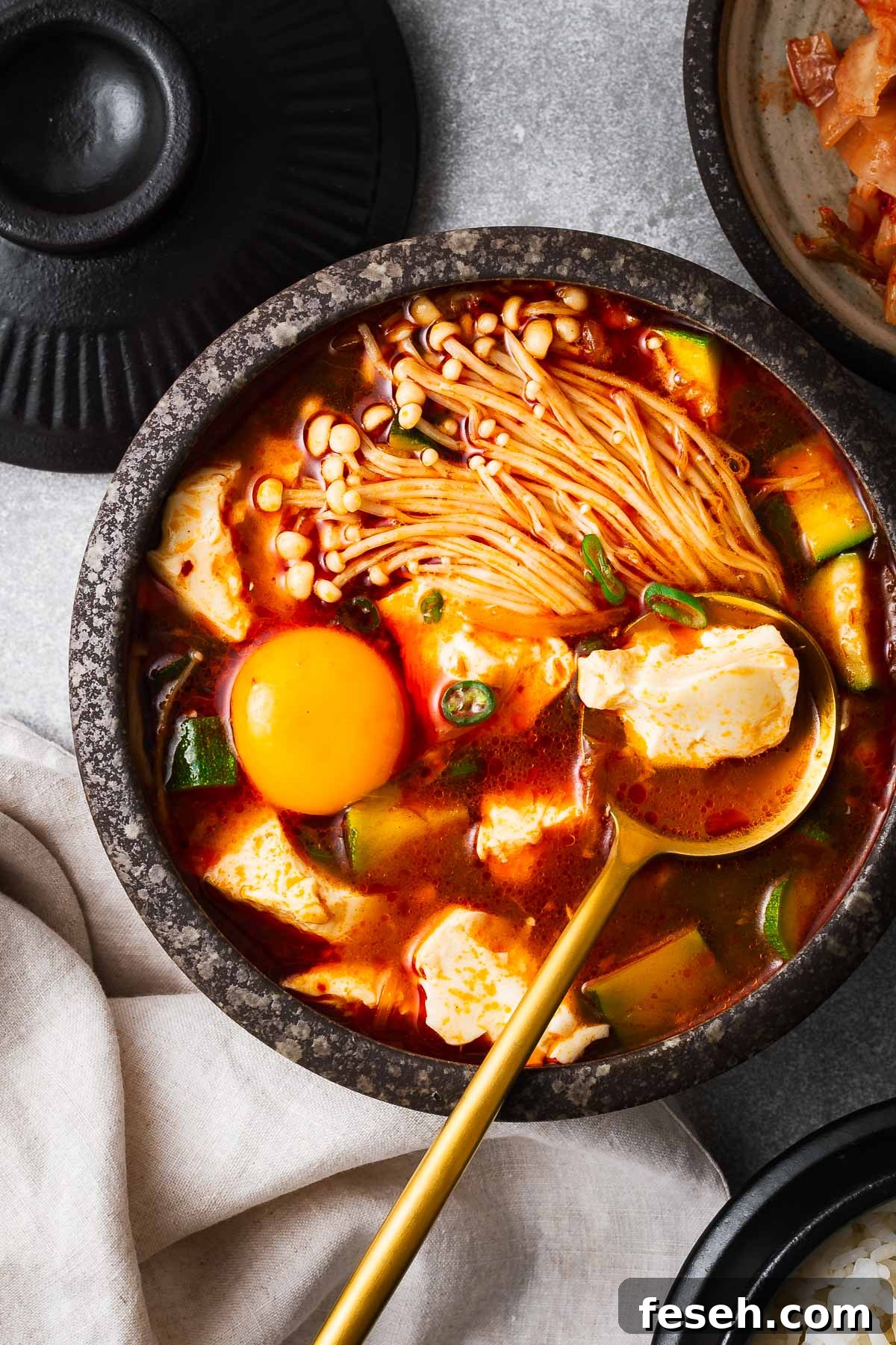 A bowl of Korean soft tofu soup with enoki mushrooms and an egg yolk.