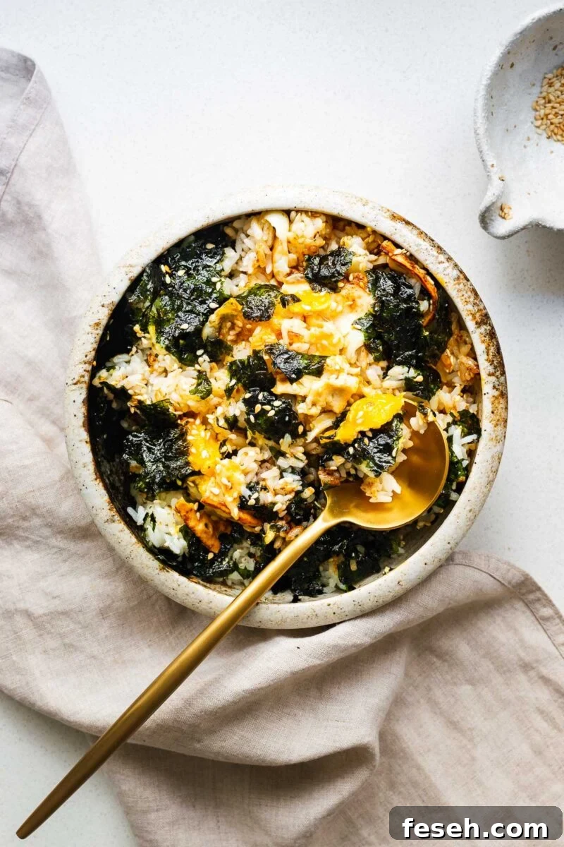 A bowl of gyeran bap with everything mixed together using a golden spoon. The runny yolk coats the plump rice kernels.
